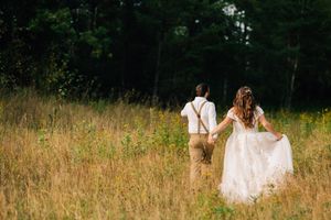 A bride and groom walking through a sun-lit meadow of tall grass.