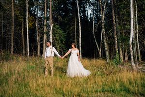 A bride and groom stand together in a forest clearing surrounded by tall trees.
