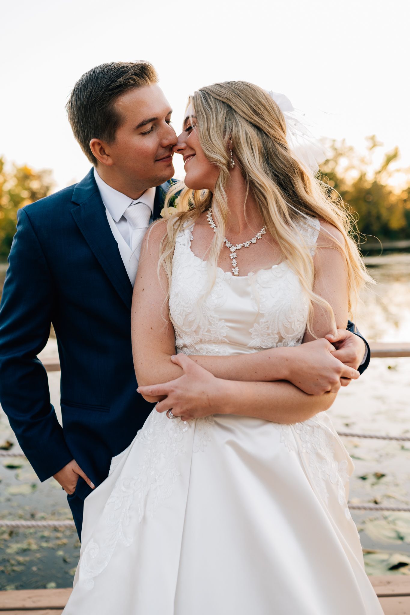 Newlywed couple shares intimate moment on rustic dock during golden hour sunset photoshoot.