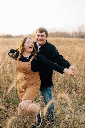 A playful couple laughs together while embracing in a golden field of dried grass.
