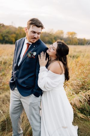 A couple shares a romantic moment in a golden field at sunset, with the bride in white and groom in navy.