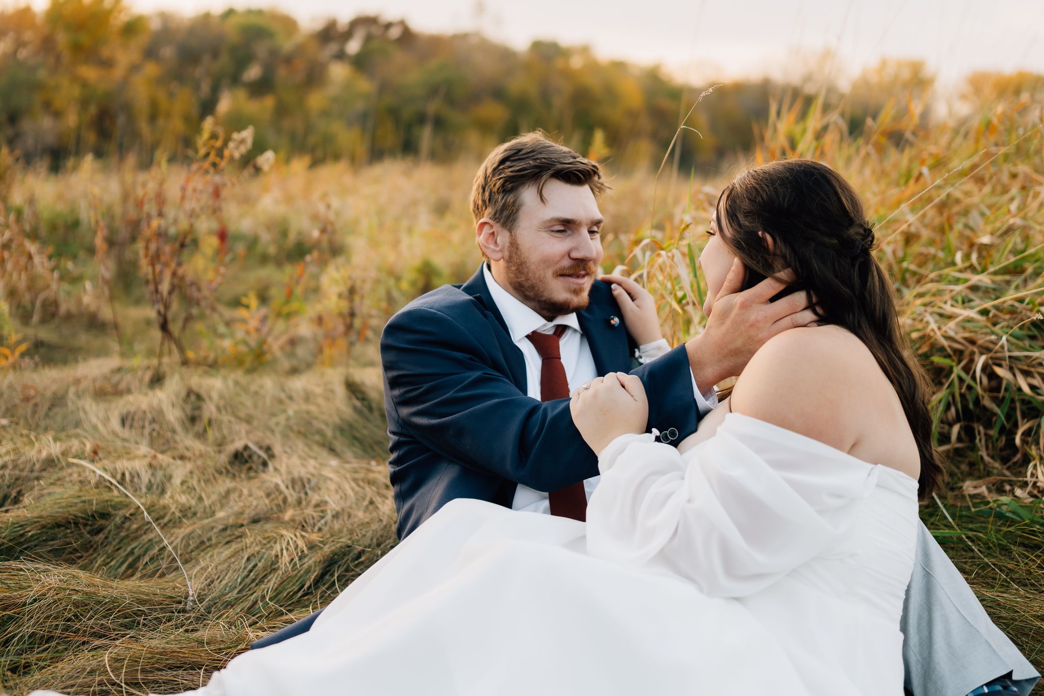 A couple shares an intimate moment together in a sunlit field of tall golden grass during their wedding photoshoot.