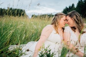 Two people in white dresses share an intimate moment while laying in a wildflower meadow.