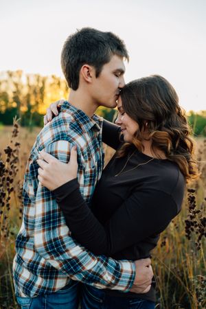 Romantic couple embracing in plaid shirts against sunset backdrop in field.