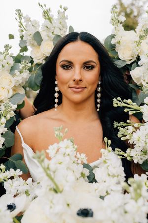 Beautiful bride surrounded by white floral arrangements and eucalyptus leaves in an outdoor portrait.