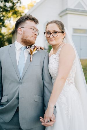 A tender wedding portrait of a couple in formal attire standing by a church.