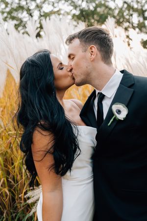 Romantic wedding couple sharing an intimate kiss against a backdrop of golden ornamental grasses.