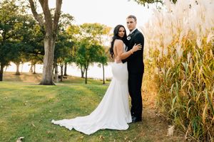 Wedding couple poses near tall cornfield at sunset in outdoor rustic setting.