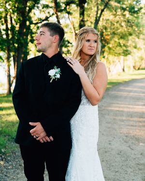 Newlyweds share an intimate moment on a tree-lined path during golden hour.
