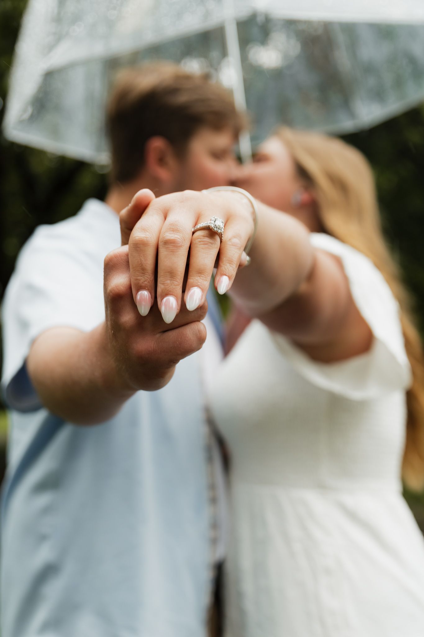 Close-up of newlyweds' hands showing off wedding rings against a blurred outdoor background.