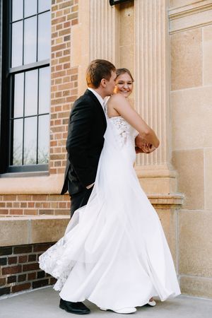 Wedding couple dancing and twirling on brick building patio with classical columns.