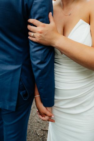 Close-up details of newlyweds embracing, showing white dress and navy suit.