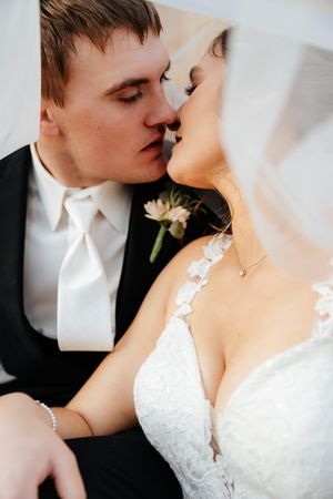 Intimate close-up of newlyweds kissing, with groom in black tuxedo and bride in lace wedding dress.