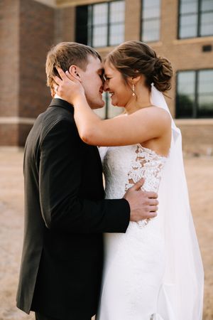 Intimate wedding portrait of couple embracing against brick building exterior.