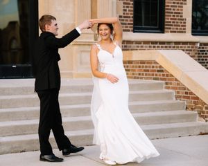 Newlyweds sharing romantic dance moment on outdoor steps of brick building.