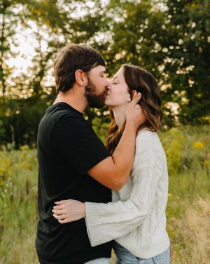 Romantic couple embracing and kissing in a sunlit field with tall grass.