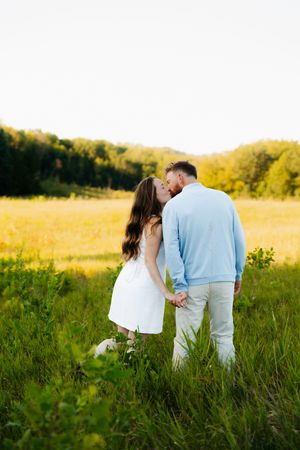 A couple shares an intimate moment in a golden sunlit meadow during sunset.