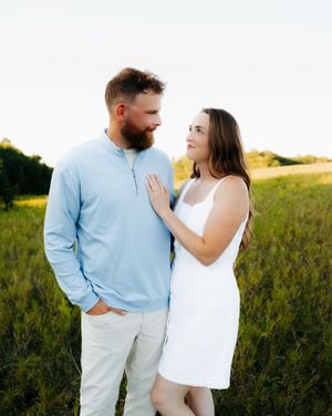 A couple in casual attire shares tender moments while walking through a sunlit field at sunset.