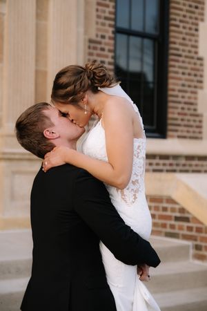 Romantic wedding couple sharing intimate kiss on stone steps of brick building.