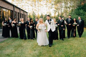 Wedding party in black and white attire posing together outdoors with trees in the background.