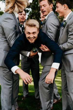 Groomsmen in gray suits share a candid laughing moment together outdoors.