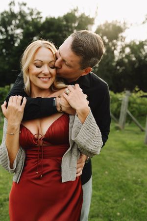 Intimate couple shares tender moments in a garden setting with her wearing a red dress and grey cardigan.
