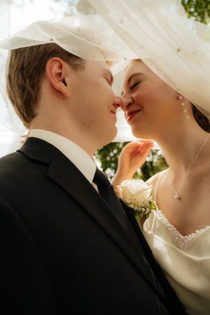 A romantic wedding couple shares an intimate moment under a veil during their outdoor ceremony.