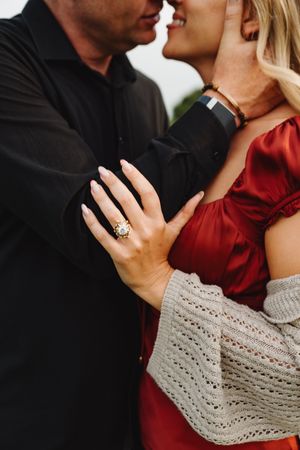 Close-up engagement photo showing couple in black and red with diamond ring visible.