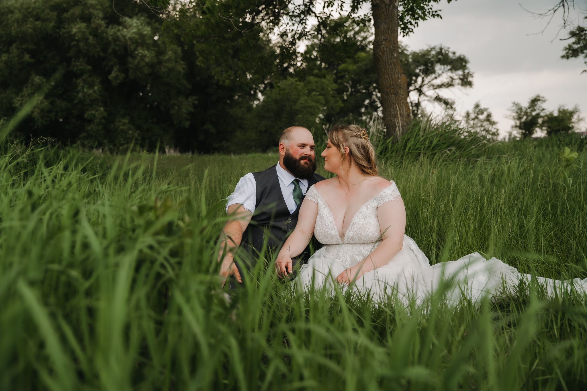 A couple sits together in tall green grass during a romantic outdoor photo session.