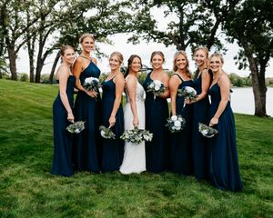 Wedding party in navy blue dresses and white bouquets posing together on a grassy hillside.