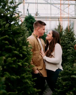 A romantic couple shares an intimate moment among evergreen Christmas trees at a tree farm.