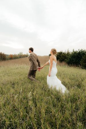 A couple walks hand in hand through a rustic field on their wedding day.