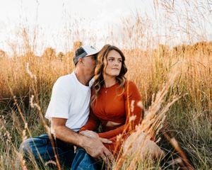 A couple shares an intimate moment among tall autumn grass during sunset.
