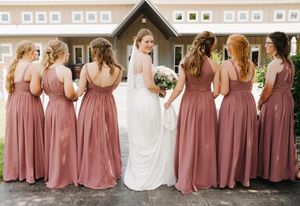 Wedding party in dusty rose dresses lined up against neutral building exterior.