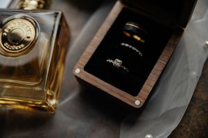 Wedding rings and perfume bottle arranged on dark surface for detail shot.