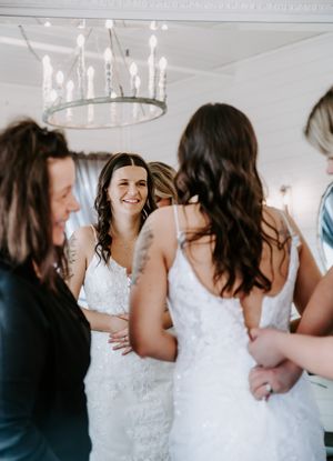 Wedding scene with women in white dresses gathered under an elegant chandelier.