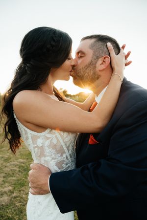 Romantic wedding couple sharing intimate kisses at sunset in a grassy field.