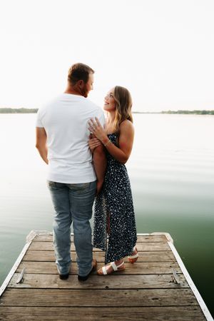 Couple sits together on wooden dock overlooking serene lake at sunset.