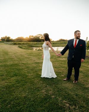 Wedding couple dancing and twirling in an open grassy field at sunset.