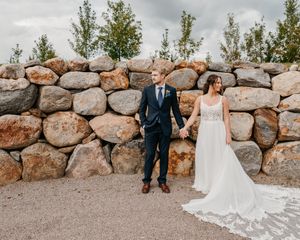 Couple posing for romantic wedding photos against a rustic stone wall backdrop in an outdoor setting.