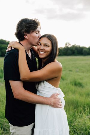 Couple shares joyful embraces in a sunny meadow with tall grass.