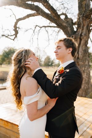 Romantic wedding portrait under a large tree with soft sunlight filtering through branches.