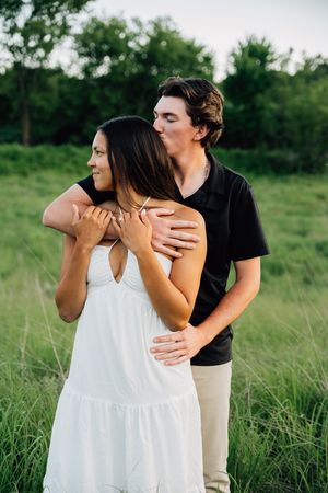 A couple shares tender moments in a summer meadow, with her wearing a flowing white dress.
