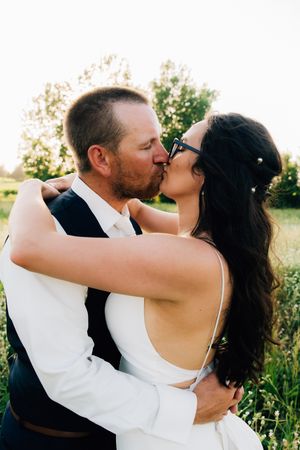 A romantic couple shares intimate kisses in a sunlit field during their wedding photoshoot.