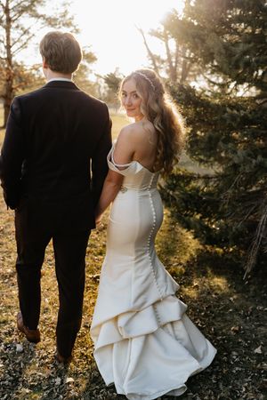 A couple in wedding attire poses together during golden hour in a forest setting.