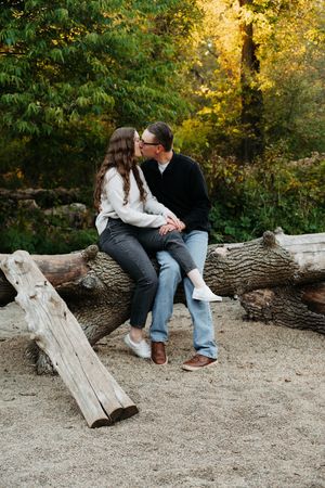 Romantic couple sitting together on fallen logs in a golden-lit forest setting.