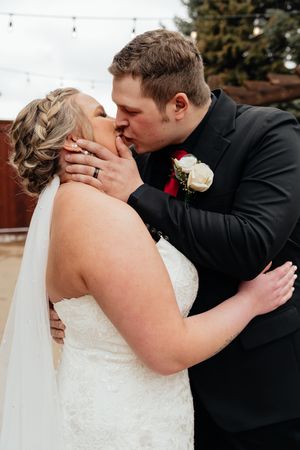 Newlywed couple sharing a passionate kiss outdoors while wearing formal wedding attire with white dress and black suit.