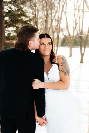 Romantic winter wedding portrait of couple in snowy forest setting with bride in white dress.
