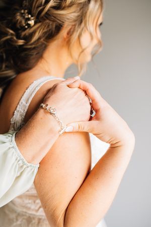 Close-up of a delicate crystal bracelet on a bride's wrist against a light-colored dress background.