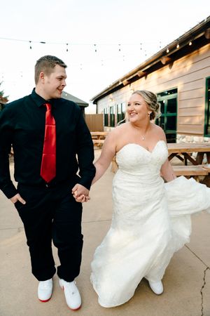 A joyful wedding couple walking outside, with the bride in white and groom wearing a red tie.